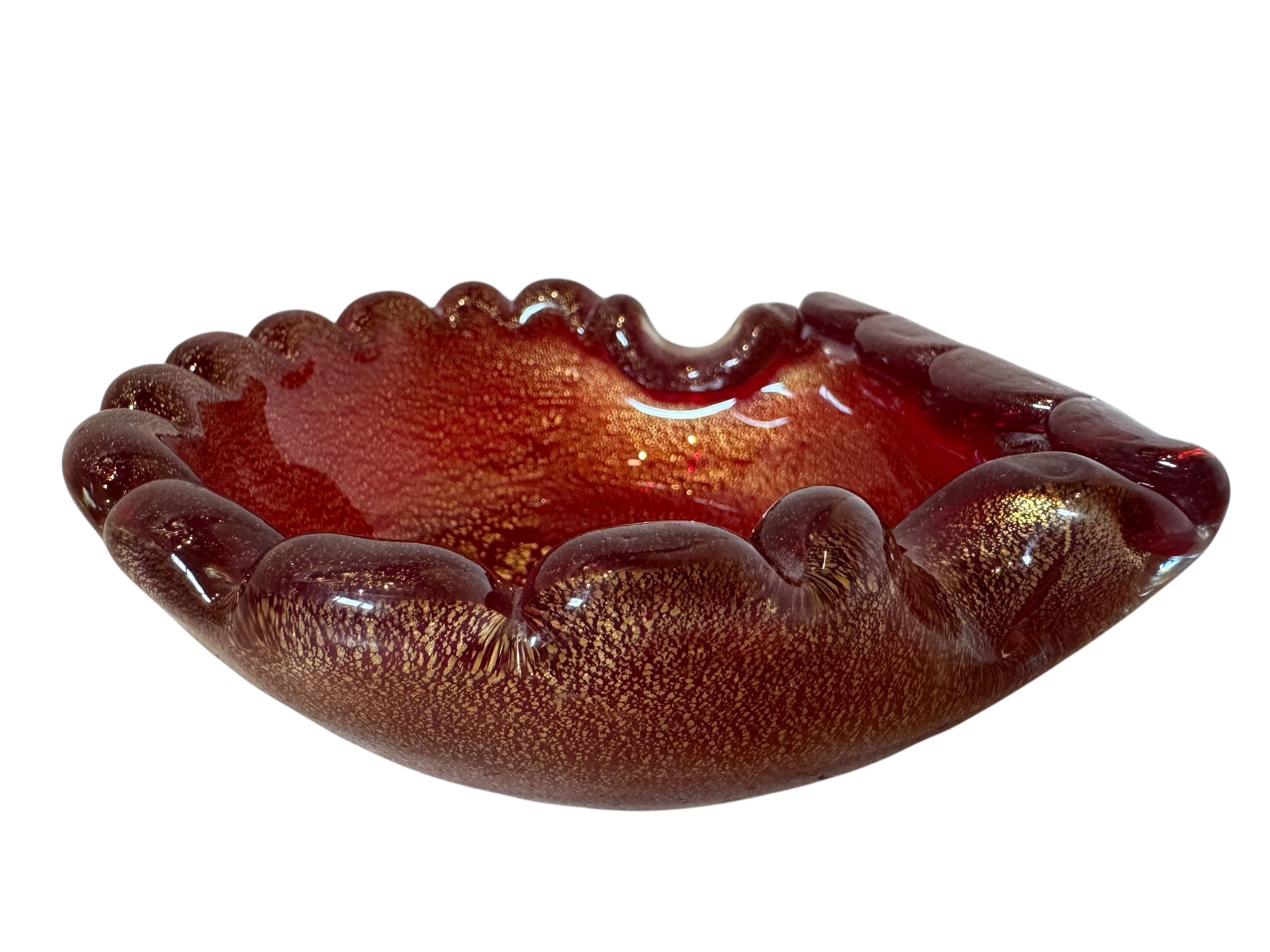 A handcrafted Murano glass bowl with a ruffled edge, deep red color, and gold specks created using the "oro zecchino" technique. The surface has a crackled gold pattern that reflects light, making it a striking decorative piece.