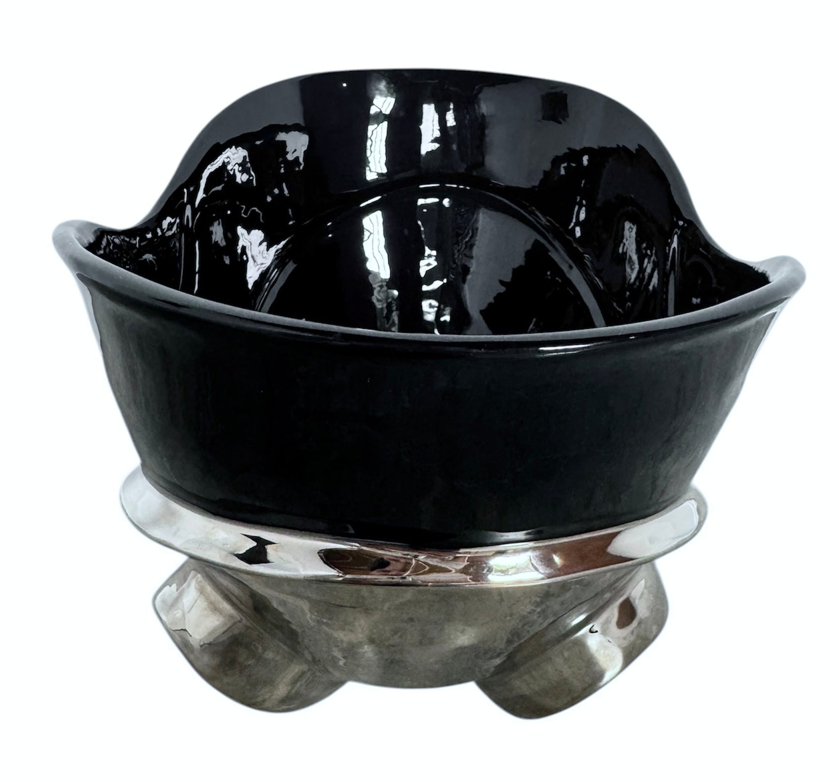 A large, decorative ceramic bowl by Dolbi Cashier in a dramatic Postmodern style. The top half is finished in a polished, piano-black glaze with an organic, wavy "butterfly" rim that dips in the center and rises at the sides. The bottom half is finished in a reflective, metallic silver chrome glaze, featuring bold, geometric-rounded feet and a structured base that appears to "hold" the black vessel. The overall shape is wide and sculptural, reminiscent of 1980s Art Deco Revival.