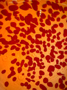 A hand-blown Italian Murano glass vase featuring a wide, bulbous body and a short, flared rim. The glass is a vibrant, translucent amber-orange base decorated with an organic "macchia" or spotted pattern of deep ruby red blotches. The red spots are elongated and vertical near the neck, becoming larger and more rounded toward the base. The surface has a high-gloss, reflective finish, showcasing mid-century modern craftsmanship.
