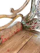 A pair of antique, heavily carved Anglo-Indian style throne chairs featuring lion figures as legs and arm supports, and peacock motifs on the backrests. The chairs have a distressed, multi-colored painted finish.