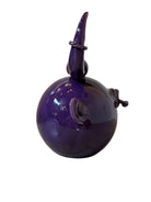 Glossy purple ceramic sculpture featuring a round body and stylized bull horns adorned with rings, and a nose ring. The sculpture has no eyes, but suggests a smiling expression.