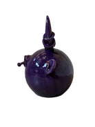 Glossy purple ceramic sculpture featuring a round body and stylized bull horns adorned with rings, and a nose ring. The sculpture has no eyes, but suggests a smiling expression.