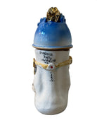 Handcrafted ceramic sculpture in the shape of a foot, decorated with intricate black and white patterns, 24KT gold accents, and topped with a blue lid featuring a gilt fish and head emerging from stylized waves.