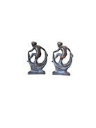 Two cast iron bookends in the Art Deco style. Each features a nude female figure leaning gracefully with one leg extended, posed atop a stylized wave or drape. The bookends have a bronze-colored finish and a vintage appearance.