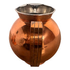 The set includes a large, rectangular, hammered copper tray with geometric openwork handles. Resting on the tray is a tall, slightly tapered copper coffee pot with a wooden handle, a matching smaller creamer pitcher with a similar wooden handle, a lidded sugar bowl, and a tiny matching metal cup or jigger. To the right off the tray sits a large, spherical copper water pitcher or jug with a wide mouth and ice lip.