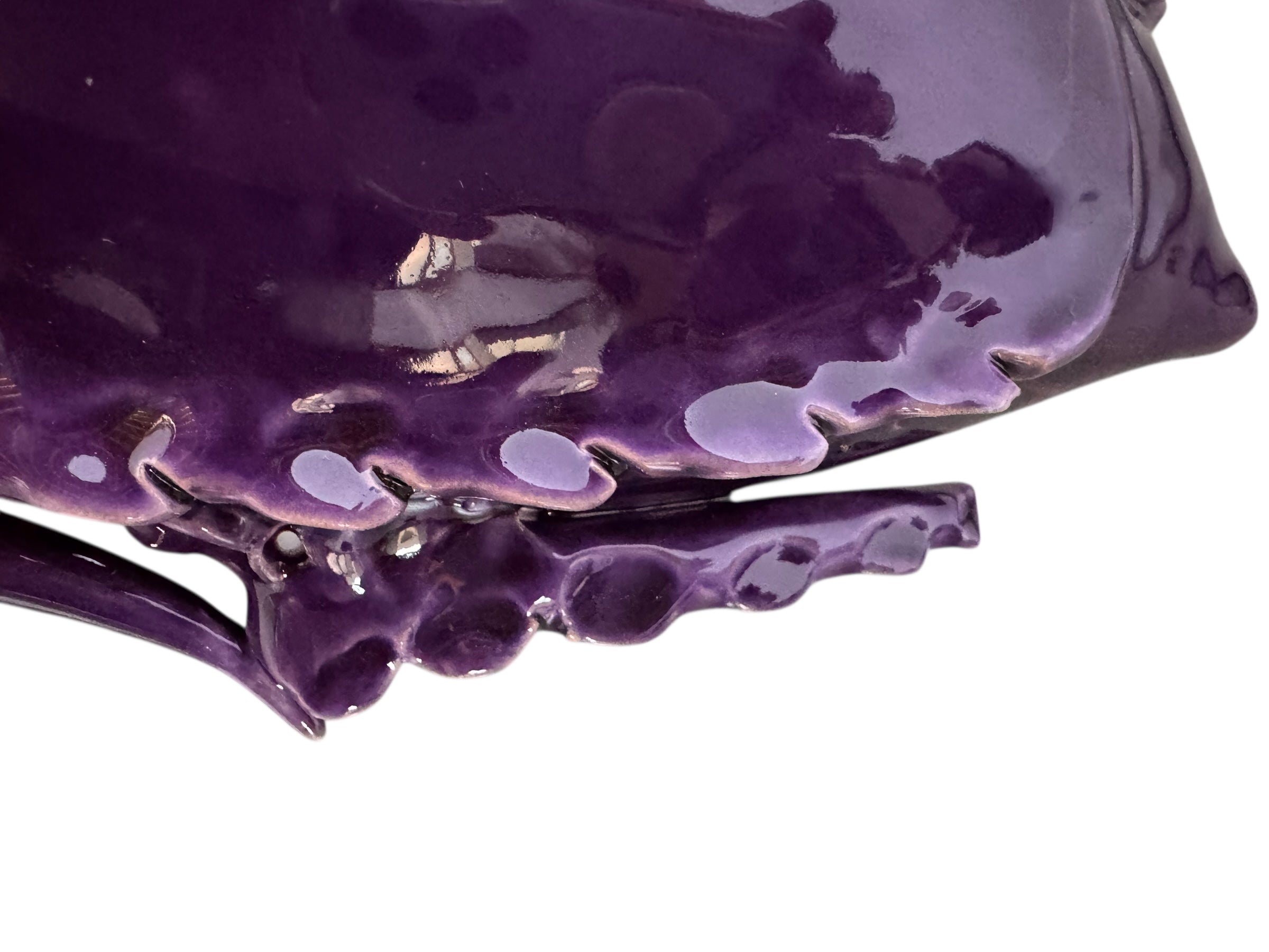 A glossy, deep purple ceramic sculpture of a beetle by Enza Fasano. The piece features a highly stylized and ornate design, blending insect-like anatomy with fantastical elements. It has a smooth, rounded shell and elongated, curved mandibles and appendages lined with sharp, thorn-like protrusions. The monochromatic glaze is reflective, highlighting the intricate sculptural details and textures of the avant-garde artwork.