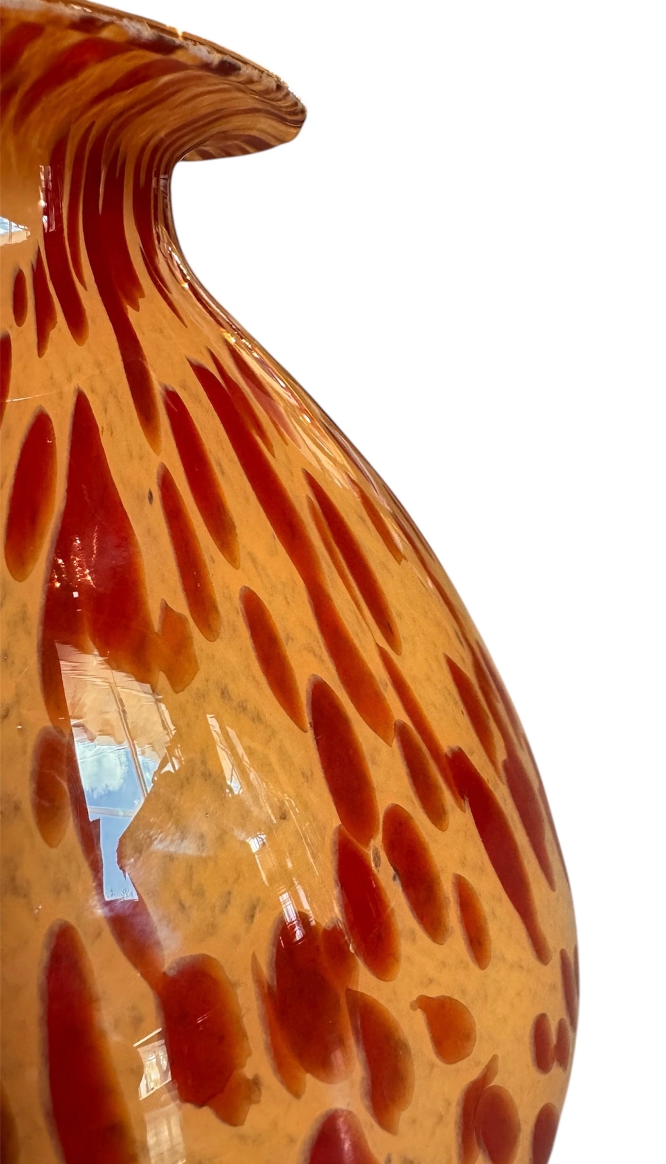 A hand-blown Italian Murano glass vase featuring a wide, bulbous body and a short, flared rim. The glass is a vibrant, translucent amber-orange base decorated with an organic "macchia" or spotted pattern of deep ruby red blotches. The red spots are elongated and vertical near the neck, becoming larger and more rounded toward the base. The surface has a high-gloss, reflective finish, showcasing mid-century modern craftsmanship.
