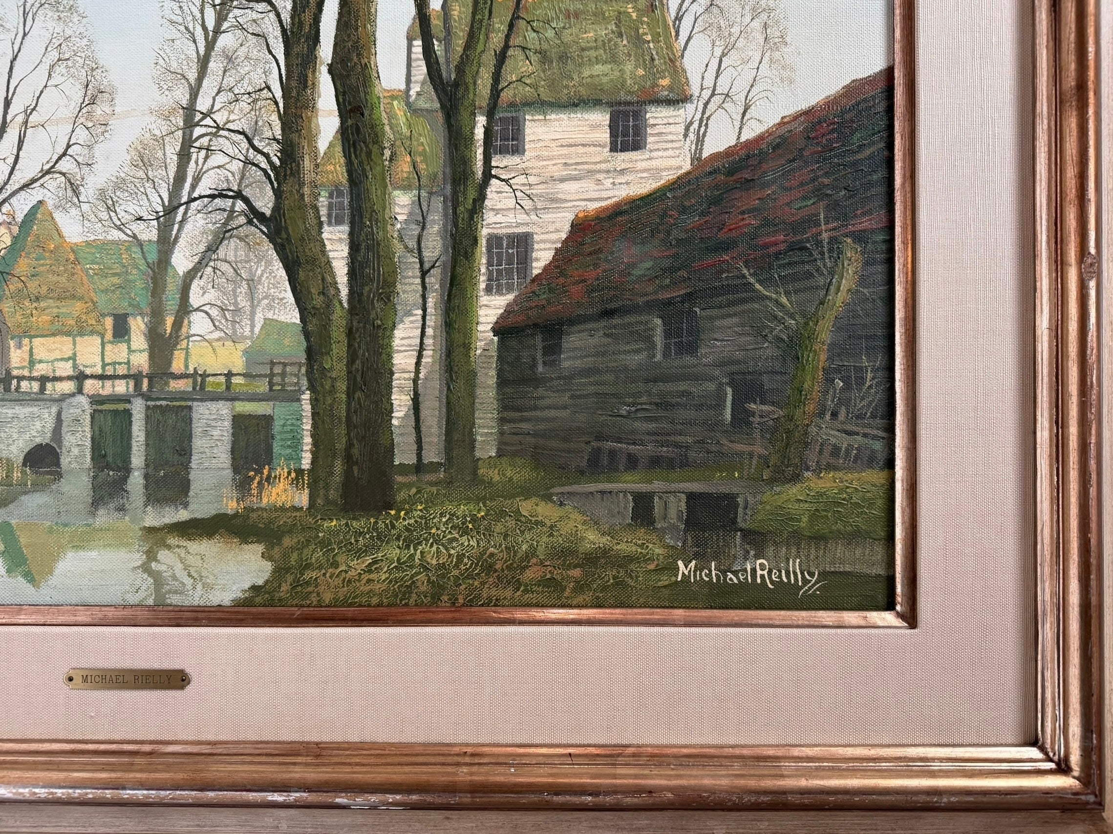 A naturalistic landscape oil painting by Michael Reilly titled "Mill Pond with Bridge" depicts a small town scene with a stone bridge over a mill pond, several buildings, and numerous bare trees under a grey sky