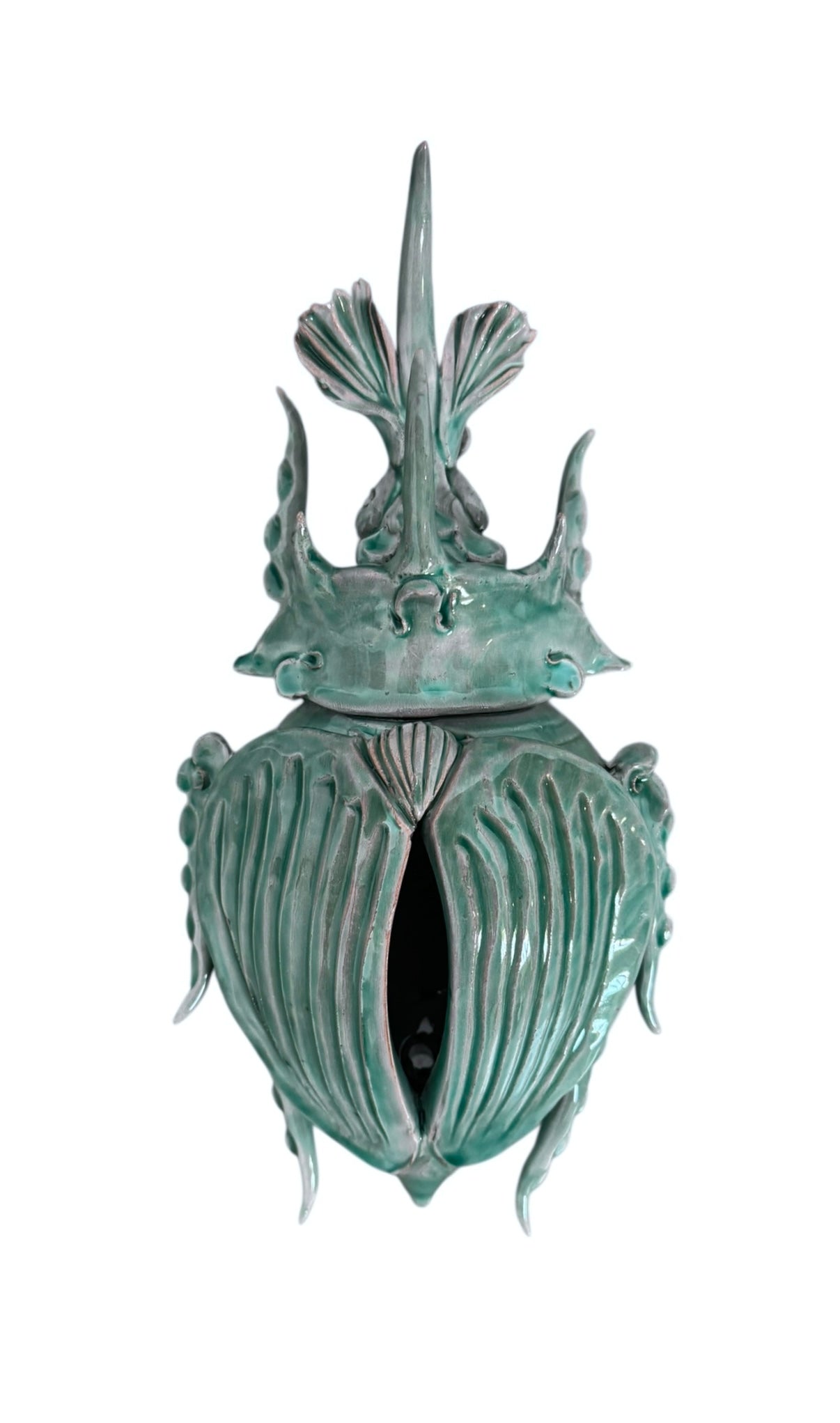 A ceramic sculpture of a stylized beetle by Enza Fasano, featuring a deep emerald green glaze with dark, metallic bronze-colored accents. The beetle is depicted with a highly textured, ribbed shell (elytra) and prominent, curved horns. Its legs are stylized with suckers, reminiscent of octopus tentacles. The piece has a glossy finish and rests against a plain white background.