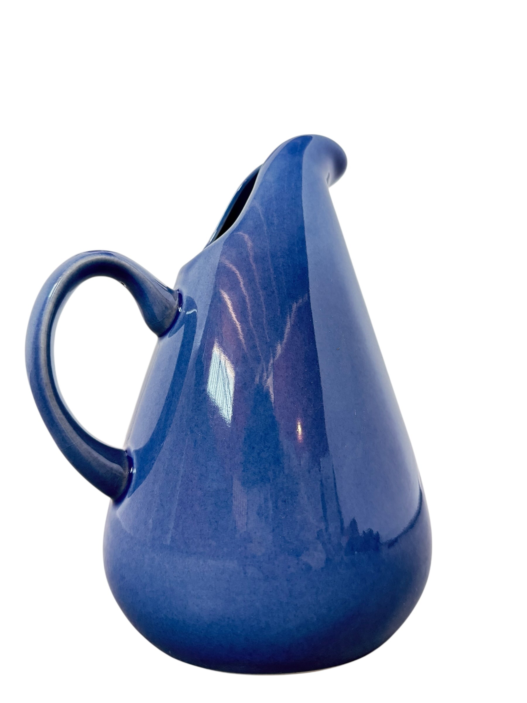 A Russel Wright American Modern stoneware water pitcher in a glossy Manitoga blue glaze is centered against a white background. The pitcher has a teardrop shape, a large handle, and a wide spout