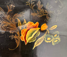 A vintage rectangular toleware serving tray with a scalloped, wavy edge and a black lacquered finish. The tray features hand-painted floral motifs in a traditional folk-art style. At the bottom center is a large, vibrant cluster of yellow and orange roses and daisies with green leaves. Smaller floral sprays and delicate gold filigree scrollwork decorate the corners and the upper rim. The center of the tray is open black space, showing light surface wear and minor scuffing consistent with age.