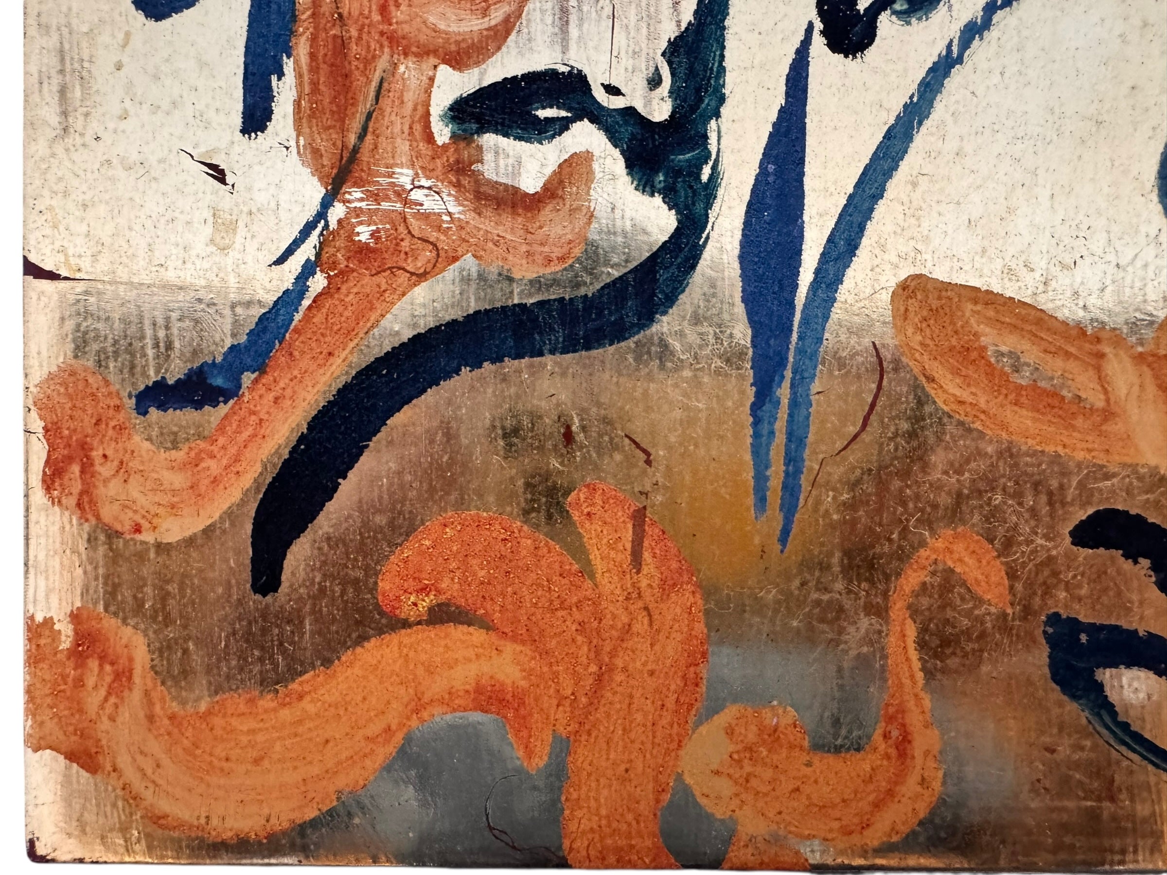 An abstract mixed-media painting on a vertical rectangular panel with a reflective, metallic gold and copper background. The composition features fluid, expressive brushstrokes in warm orange, ochre, and deep blue.
The orange strokes are thick and organic, resembling swirling flames or floral petals, while the blue marks consist of thin, lyrical lines and looped scribbles that dance across the surface. The metallic substrate is visible through the translucent paint, creating a play of light and texture