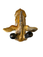 A hand-painted, cast resin sculpture of a seated giraffe. The giraffe has a long neck, is predominantly gold with light markings, and is in a resting pose. The sculpture is against a plain white background