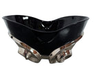 A large, decorative ceramic bowl by Dolbi Cashier in a dramatic Postmodern style. The top half is finished in a polished, piano-black glaze with an organic, wavy "butterfly" rim that dips in the center and rises at the sides. The bottom half is finished in a reflective, metallic silver chrome glaze, featuring bold, geometric-rounded feet and a structured base that appears to "hold" the black vessel. The overall shape is wide and sculptural, reminiscent of 1980s Art Deco Revival.