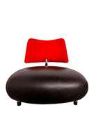 A Leolux Pallone armchair with a large, black, spherical leather seat and a smaller, red, curved leather backrest, supported by short metal legs.