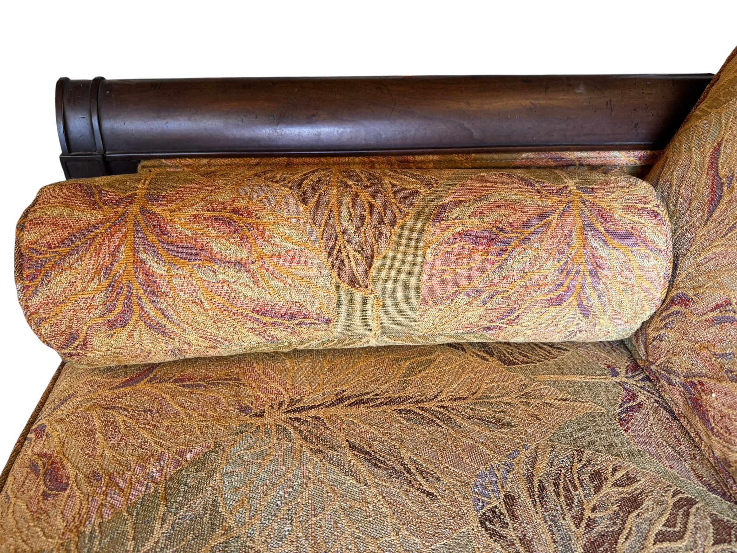 A Neoclassical-style wooden loveseat with a dark mahogany frame featuring scrolled arms and tapered legs. The upholstery consists of plush cushions and two matching cylindrical bolster pillows, all covered in a golden-yellow jacquard fabric with a large-scale, repeating autumnal leaf pattern in shades of muted orange and brown.