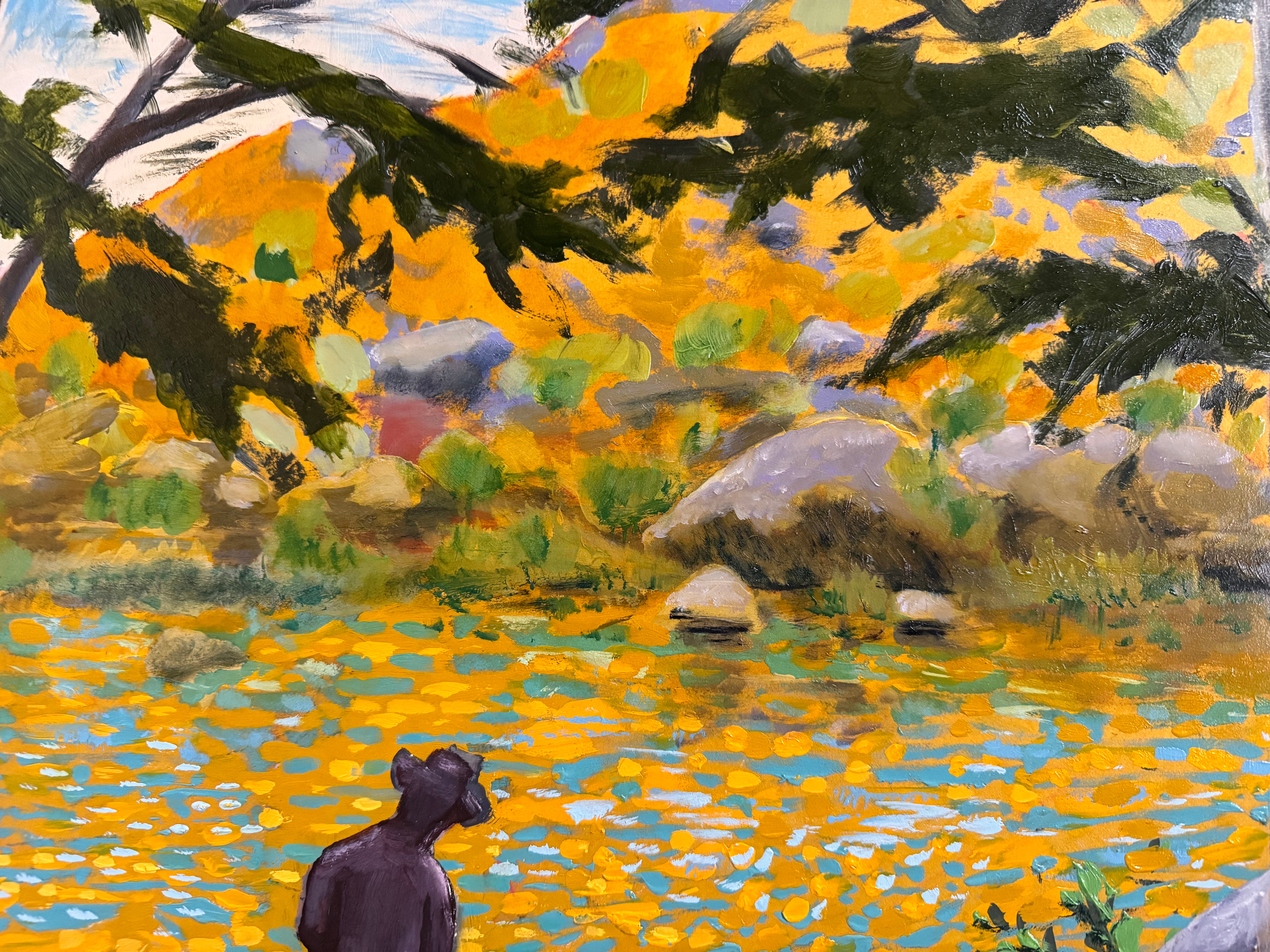 A vibrantly colored landscape painting titled 'Perdernales Falls Fisherman,' featuring two large trees with prominent exposed roots framing a body of water. A lone figure, a fisherman, stands by the water in the middle ground. The painting uses bold strokes of yellow, green, red, and blue, and is enclosed in a rustic dark wooden frame with a light-colored inner mat.