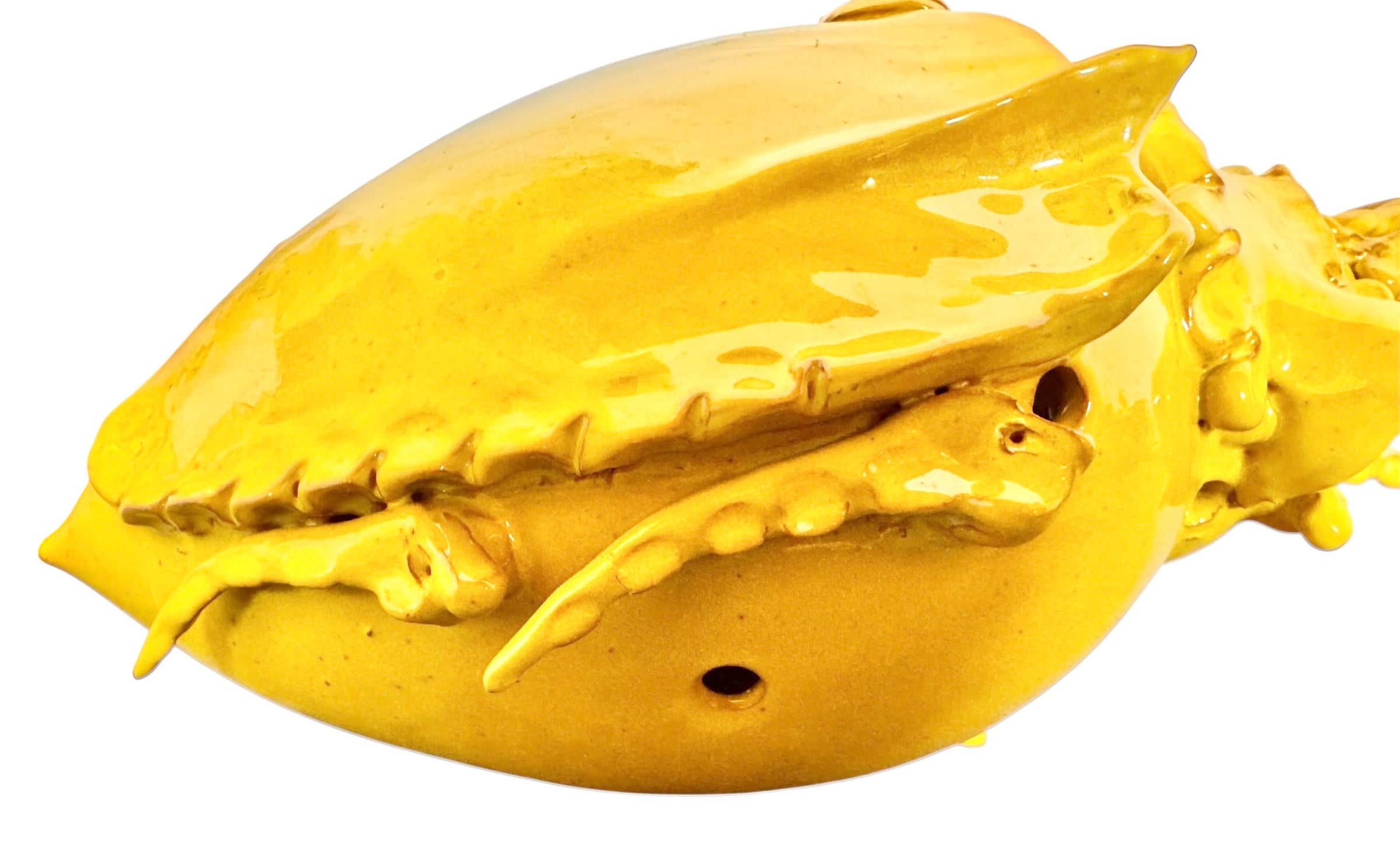 a large, high-gloss ceramic sculpture by Enza Fasano, shaped like a stylized beetle. The entire piece is finished in a warm, honey-yellow glaze. The beetle features prominent, curved mandibles at the front, a textured "collar" area, and a rounded, shell-like body with decorative ridges along the edges. The surface is smooth and reflective, catching the light across its organic contours.