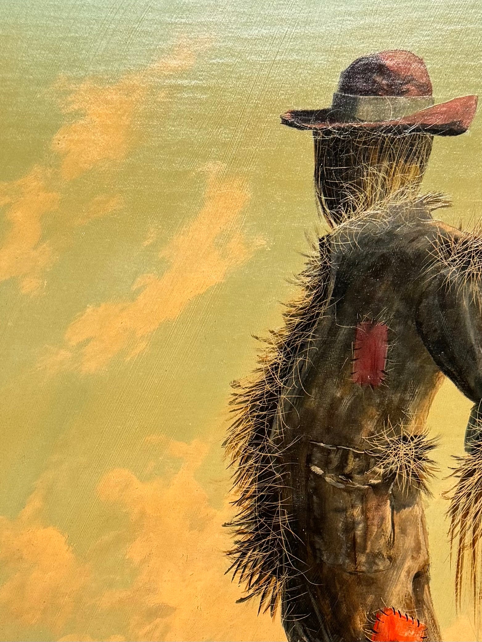 An oil painting on a wooden panel depicts a solitary scarecrow standing in a vast, grassy field under a pale yellow and blue sky. The scarecrow is shown from a three-quarters back view, wearing a brimmed hat and a tattered, patched brown coat with frayed straw bursting from its sleeves and edges. In the far left background, a long, white rustic barn sits before a dense line of green trees. The entire piece is enclosed in a thick, weathered, natural wood frame.