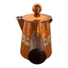 The set includes a large, rectangular, hammered copper tray with geometric openwork handles. Resting on the tray is a tall, slightly tapered copper coffee pot with a wooden handle, a matching smaller creamer pitcher with a similar wooden handle, a lidded sugar bowl, and a tiny matching metal cup or jigger. To the right off the tray sits a large, spherical copper water pitcher or jug with a wide mouth and ice lip.