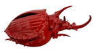 A vibrant, glossy red ceramic sculpture of a rhinoceros beetle by Enza Fasano. The piece features a highly reflective, deep crimson glaze that accentuates its smooth, rounded abdomen and the intricate, jagged textures of its head and horns.