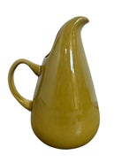 A chartreuse (yellow-green) ceramic pitcher designed by Russel Wright, featuring a teardrop shape, an elongated spout, and a curved handle