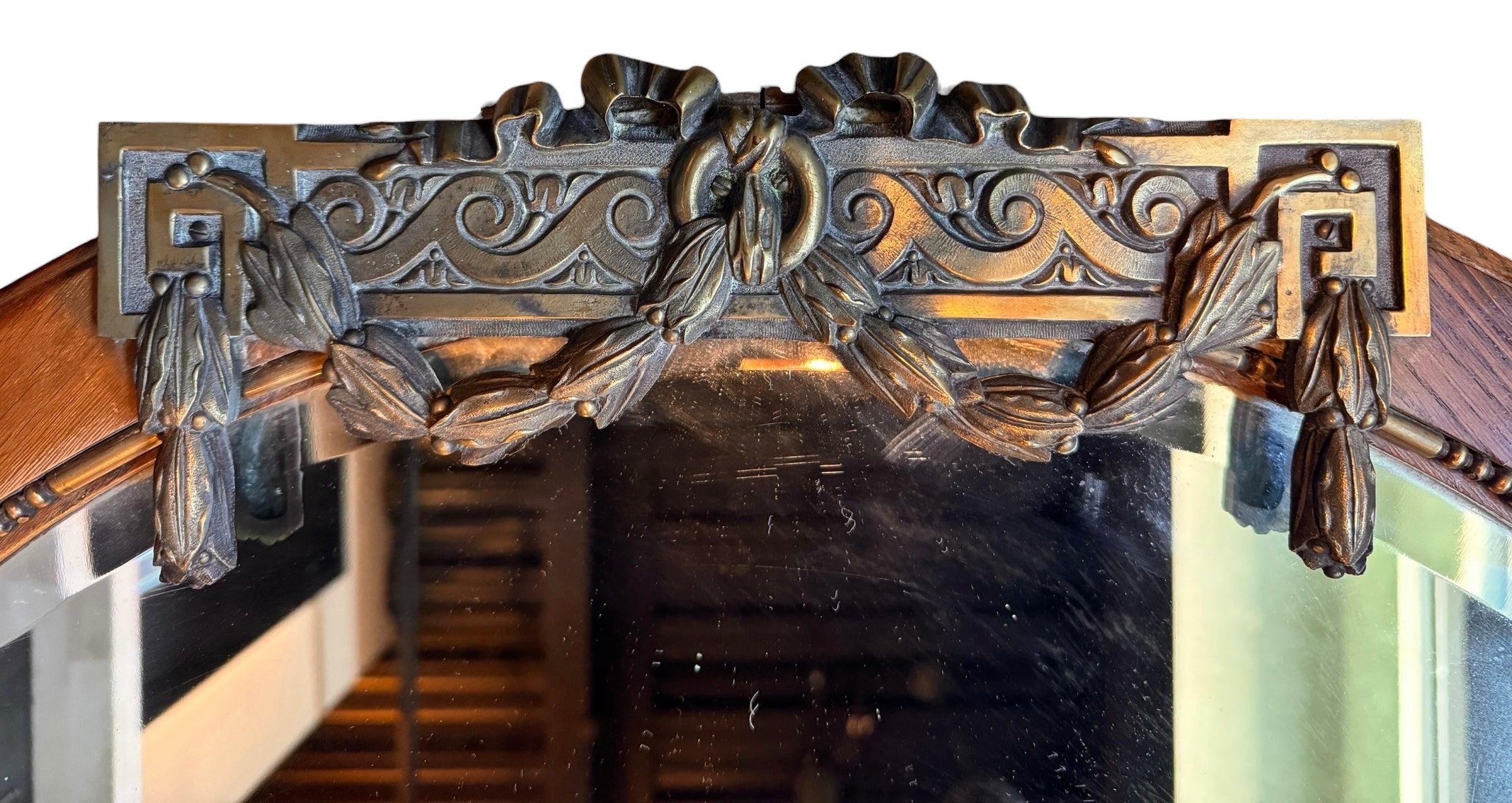 An oval-shaped mirror featuring a wooden frame and an ornate metal crest at the top.