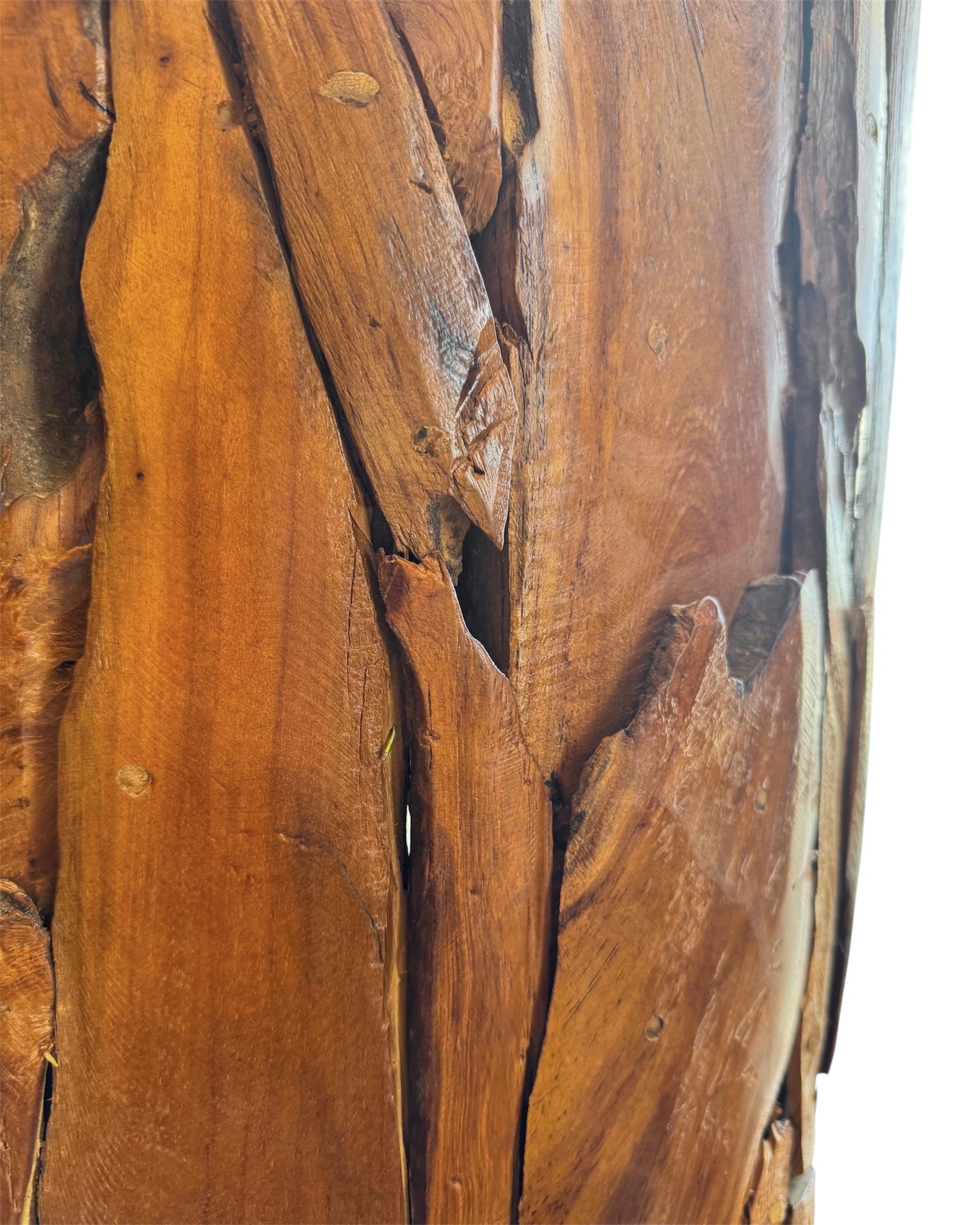 Two table lamps made from repurposed teak wood vases. The bases are tall and tapered, featuring a rugged, mosaic-like texture composed of various pieces of dark, polished teak wood with visible natural grain and crevices. Each lamp is topped with a large, warm-toned conical shade that is currently wrapped in protective clear plastic, emitting a soft, golden glow. The lamps are positioned on a clean white surface against a neutral background.
