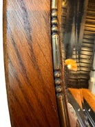 An oval-shaped mirror featuring a wooden frame and an ornate metal crest at the top.