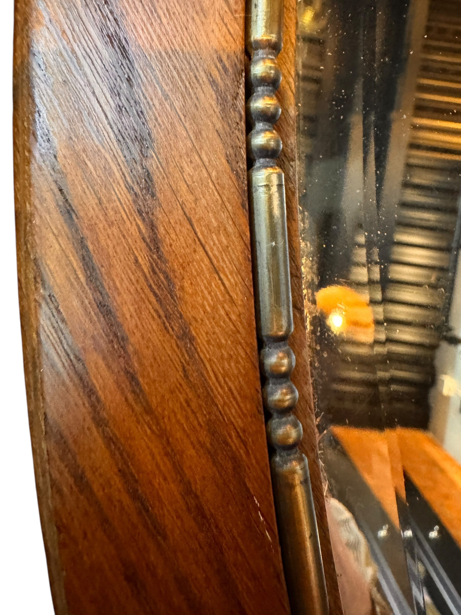 An oval-shaped mirror featuring a wooden frame and an ornate metal crest at the top.