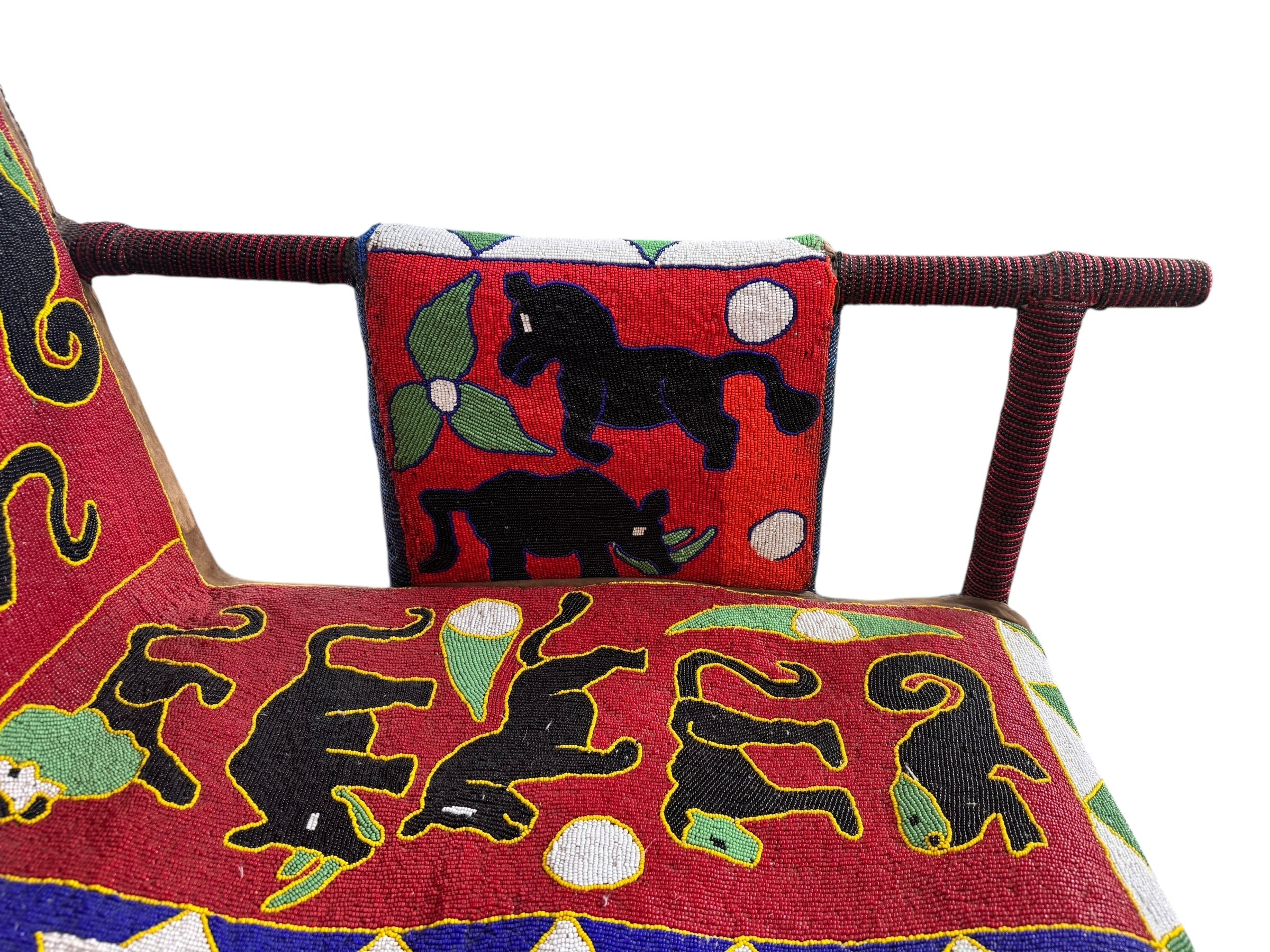 Close-up of a Yoruba beaded armchair, featuring vibrant red, blue, and green beads in a pattern of stylized masks and animals such as lions and zebras