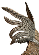 A pair of vintage, silver-plated brass fighting rooster figurines positioned in a confrontational stance against a white background. The rooster on the left is crouched low with its head down and tail feathers fanned high, while the rooster on the right stands more upright with its wings slightly flared. Both feature intricate feather detailing, a metallic patina showing hints of brass through the silver, and small, bright red glass eyes.