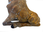 A hand-painted, cast resin sculpture of a seated giraffe. The giraffe has a long neck, is predominantly gold with light markings, and is in a resting pose. The sculpture is against a plain white background