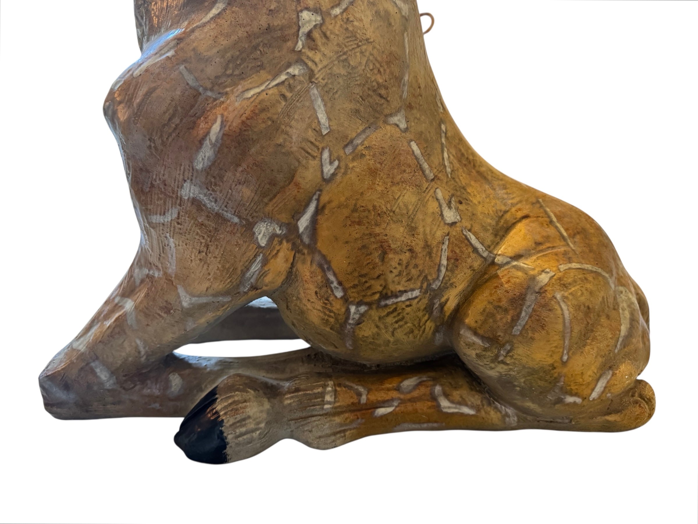 A hand-painted, cast resin sculpture of a seated giraffe. The giraffe has a long neck, is predominantly gold with light markings, and is in a resting pose. The sculpture is against a plain white background