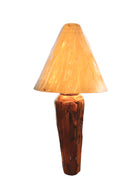 Two table lamps made from repurposed teak wood vases. The bases are tall and tapered, featuring a rugged, mosaic-like texture composed of various pieces of dark, polished teak wood with visible natural grain and crevices. Each lamp is topped with a large, warm-toned conical shade that is currently wrapped in protective clear plastic, emitting a soft, golden glow. The lamps are positioned on a clean white surface against a neutral background.

