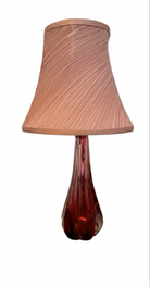 A table lamp featuring a teardrop-shaped, reddish-purple glass base and a conical, pleated, light-pink fabric shade.