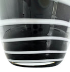 A sleek, hand-blown Polish art glass vase featuring a tall, slender neck that flares into a rounded, bulbous body. The vase is made of opaque black glass decorated with a continuous white spiral ribbon that winds around the entire piece from base to rim. The high-gloss, reflective surface creates sharp highlights, emphasizing its smooth, sculptural silhouette against a plain white background.
