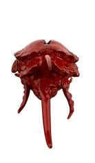 A handcrafted ceramic sculpture of a rhinoceros beetle by Enza Fasano, featuring a vibrant, glossy deep-red glaze. The piece is stylized with smooth, rounded contours and prominent, elegant horns extending forward. Its surface reflects light, highlighting the rich texture and artisanal detail of the clay.