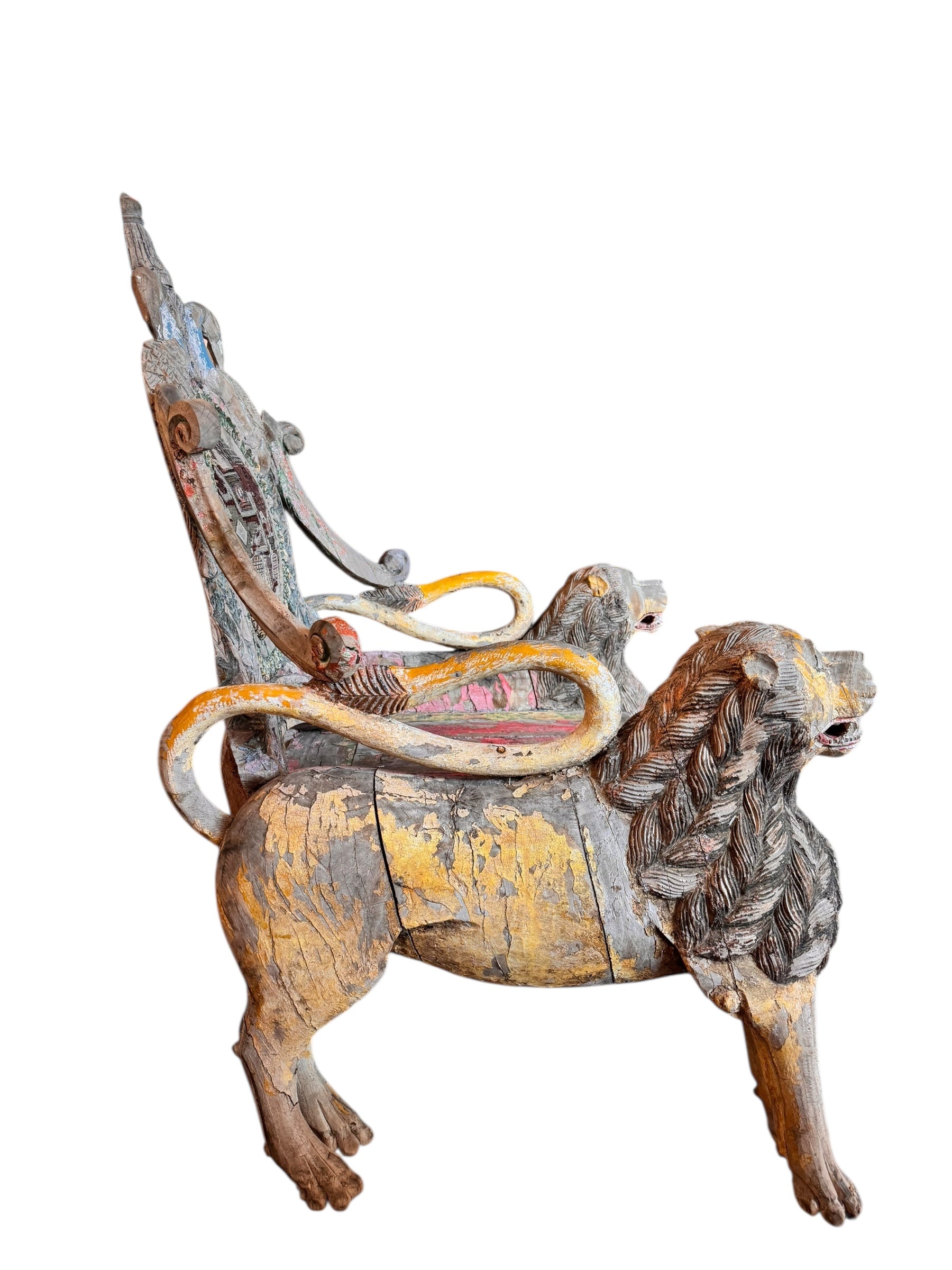 A pair of antique, heavily carved Anglo-Indian style throne chairs featuring lion figures as legs and arm supports, and peacock motifs on the backrests. The chairs have a distressed, multi-colored painted finish.