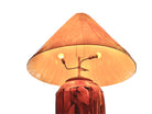 Two table lamps made from repurposed teak wood vases. The bases are tall and tapered, featuring a rugged, mosaic-like texture composed of various pieces of dark, polished teak wood with visible natural grain and crevices. Each lamp is topped with a large, warm-toned conical shade that is currently wrapped in protective clear plastic, emitting a soft, golden glow. The lamps are positioned on a clean white surface against a neutral background.
