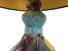 A hand-crafted ceramic table lamp featuring a vibrant, multi-colored base and a sleek black shade. The base is an upcycled artisan vase with a textured, hand-thrown appearance, decorated with geometric panels in shades of mustard yellow, forest green, cobalt blue, and burgundy, separated by thick black outlines. The lamp is topped with a minimalist, black tapered drum shade that provides a sharp contrast to the colorful, eclectic pottery below.
