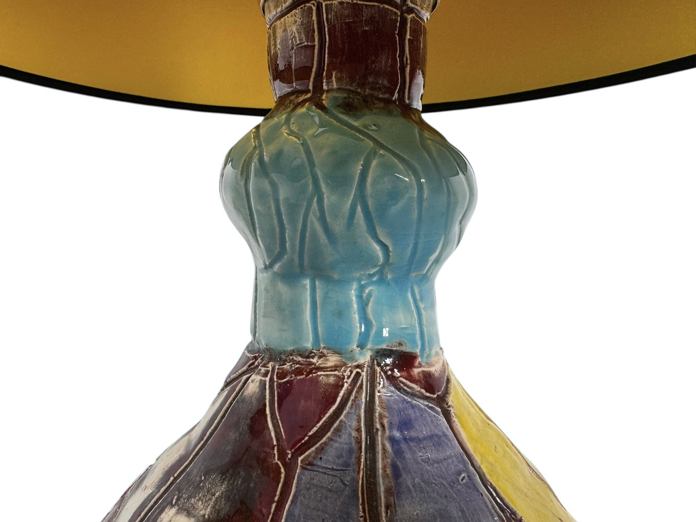 A hand-crafted ceramic table lamp featuring a vibrant, multi-colored base and a sleek black shade. The base is an upcycled artisan vase with a textured, hand-thrown appearance, decorated with geometric panels in shades of mustard yellow, forest green, cobalt blue, and burgundy, separated by thick black outlines. The lamp is topped with a minimalist, black tapered drum shade that provides a sharp contrast to the colorful, eclectic pottery below.
