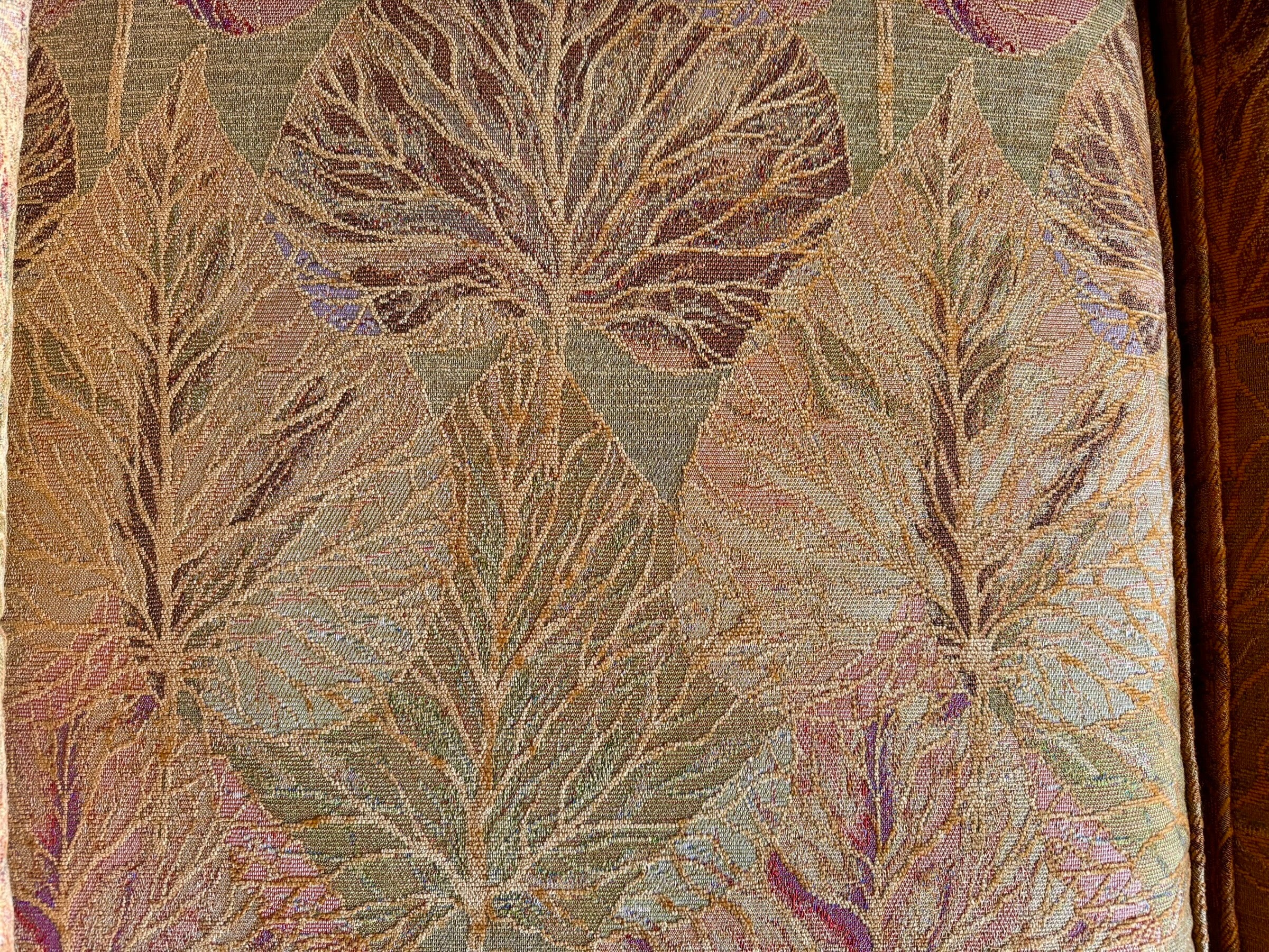 A Neoclassical-style wooden loveseat with a dark mahogany frame featuring scrolled arms and tapered legs. The upholstery consists of plush cushions and two matching cylindrical bolster pillows, all covered in a golden-yellow jacquard fabric with a large-scale, repeating autumnal leaf pattern in shades of muted orange and brown.