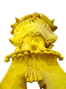 a large, high-gloss ceramic sculpture by Enza Fasano, shaped like a stylized beetle. The entire piece is finished in a warm, honey-yellow glaze. The beetle features prominent, curved mandibles at the front, a textured "collar" area, and a rounded, shell-like body with decorative ridges along the edges. The surface is smooth and reflective, catching the light across its organic contours.