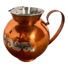 The set includes a large, rectangular, hammered copper tray with geometric openwork handles. Resting on the tray is a tall, slightly tapered copper coffee pot with a wooden handle, a matching smaller creamer pitcher with a similar wooden handle, a lidded sugar bowl, and a tiny matching metal cup or jigger. To the right off the tray sits a large, spherical copper water pitcher or jug with a wide mouth and ice lip.
