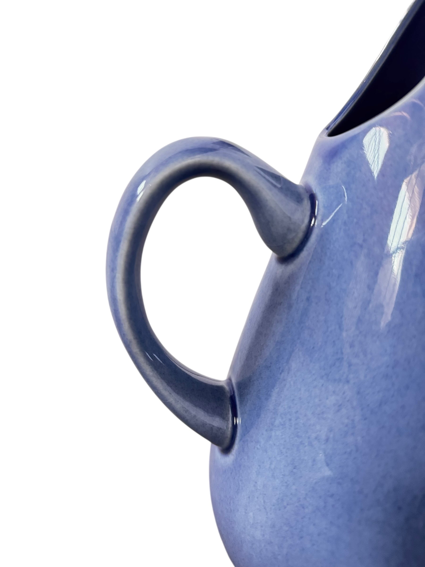 A Russel Wright American Modern stoneware water pitcher in a glossy Manitoga blue glaze is centered against a white background. The pitcher has a teardrop shape, a large handle, and a wide spout