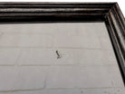 The antique Chevalier Mirror features a rectangular swing frame supported by two turned posts on decorative trestle feet. The mirror stands on four scrolled feet and features its original tarnished, silvered finish. The front of the mirror reflects a bright blue sky with wispy white clouds. The original dark brown backing is still attached to the frame.