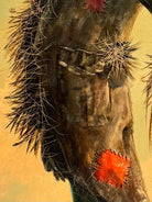 An oil painting on a wooden panel depicts a solitary scarecrow standing in a vast, grassy field under a pale yellow and blue sky. The scarecrow is shown from a three-quarters back view, wearing a brimmed hat and a tattered, patched brown coat with frayed straw bursting from its sleeves and edges. In the far left background, a long, white rustic barn sits before a dense line of green trees. The entire piece is enclosed in a thick, weathered, natural wood frame.