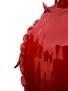 A vibrant, glossy red ceramic sculpture of a rhinoceros beetle by Enza Fasano. The piece features a highly reflective, deep crimson glaze that accentuates its smooth, rounded abdomen and the intricate, jagged textures of its head and horns.