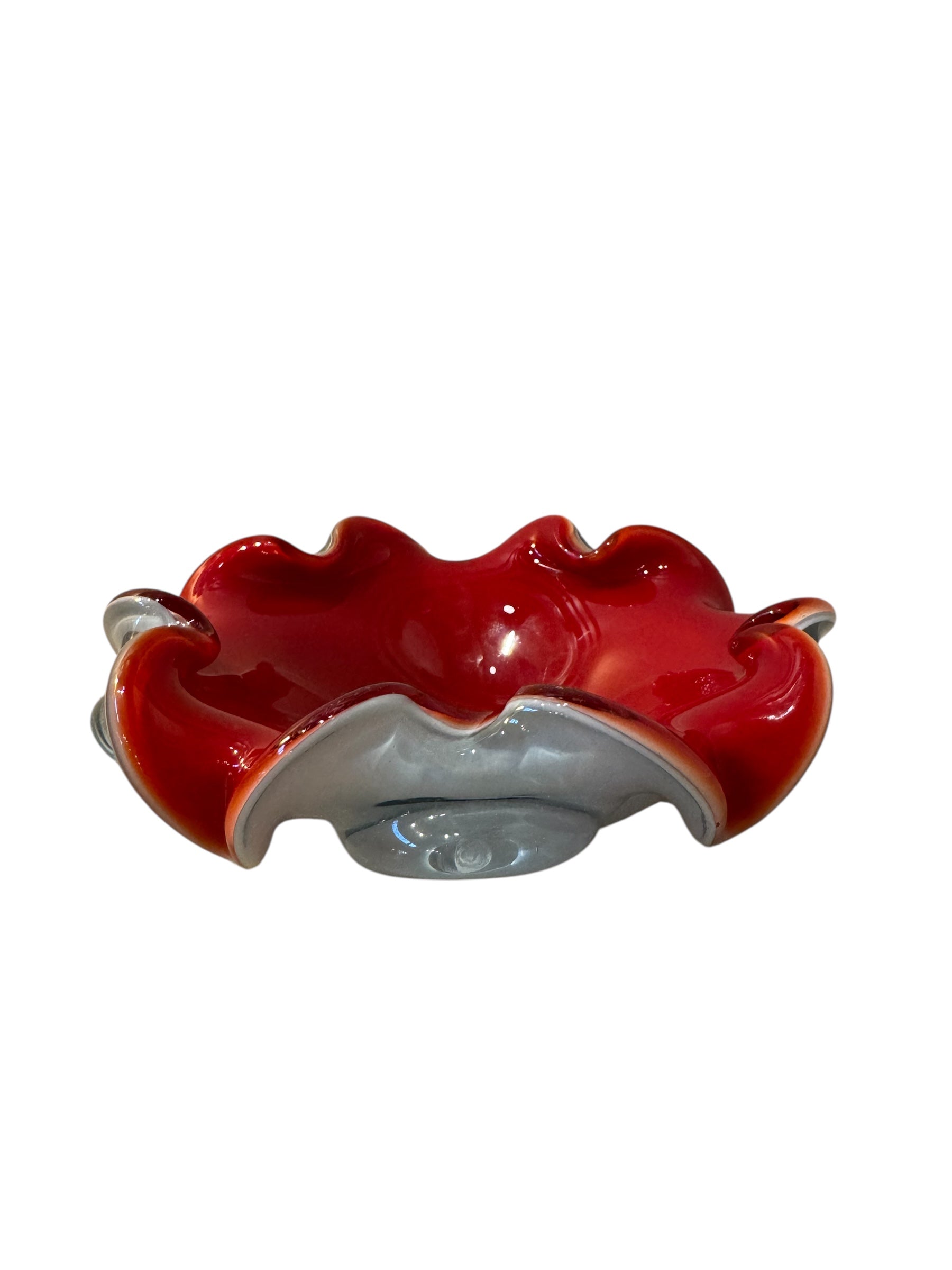 A Murano art glass bowl featuring a vibrant red interior encased in white glass, with a decorative ruffled edge. The piece is handblown, showcasing the Incamiciato technique.